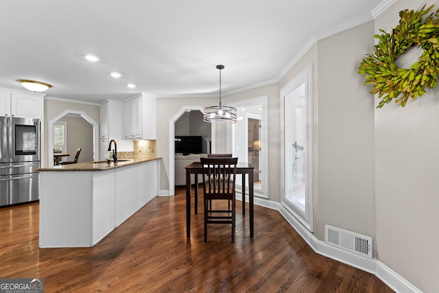 kitchen featuring visible vents, refrigerator with glass door, a peninsula, arched walkways, and white cabinets