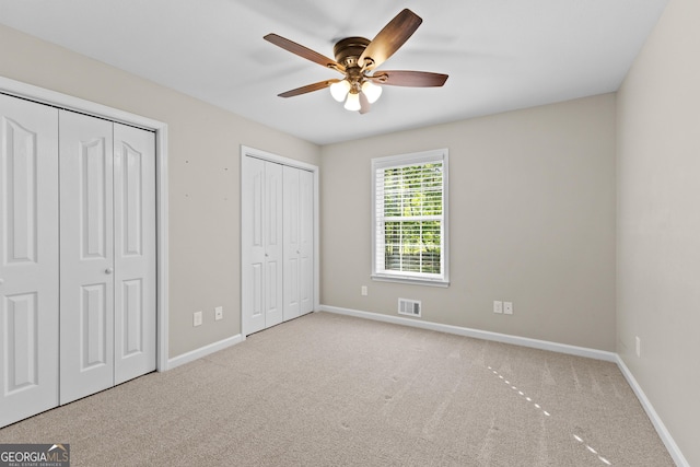 unfurnished bedroom with two closets, carpet floors, baseboards, and visible vents