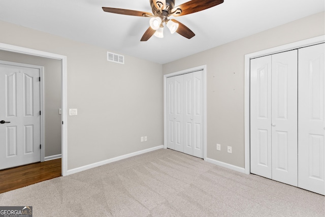 unfurnished bedroom with a ceiling fan, carpet floors, two closets, visible vents, and baseboards
