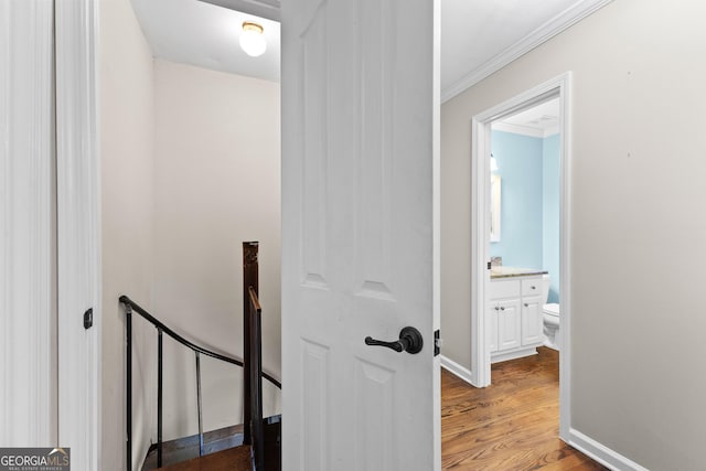 corridor with ornamental molding, baseboards, an upstairs landing, and wood finished floors