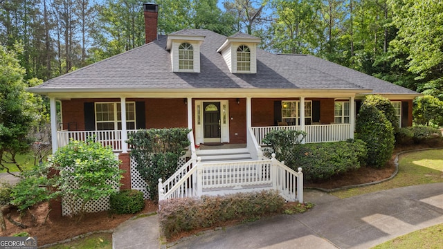 view of front facade with covered porch, a chimney, brick siding, and a shingled roof
