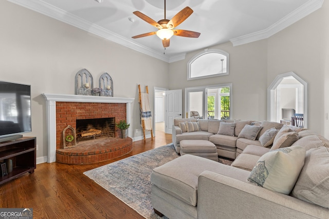 living area featuring wood finished floors, a ceiling fan, a brick fireplace, crown molding, and a towering ceiling
