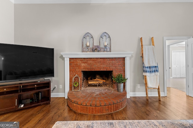 living area featuring crown molding, a brick fireplace, baseboards, and wood finished floors