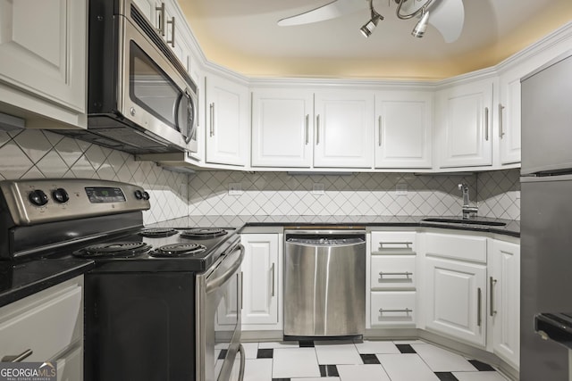 kitchen with appliances with stainless steel finishes, a sink, dark countertops, and white cabinetry