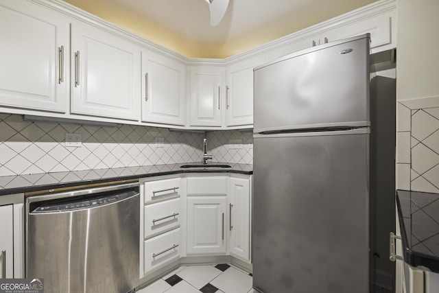 kitchen featuring stainless steel appliances, dark countertops, a sink, and white cabinetry