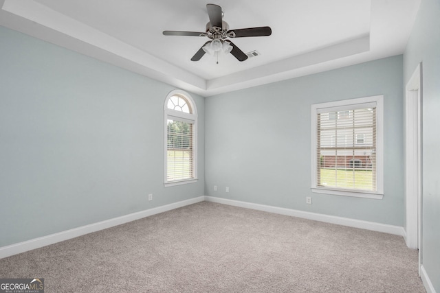 carpeted spare room with baseboards, a tray ceiling, visible vents, and a ceiling fan