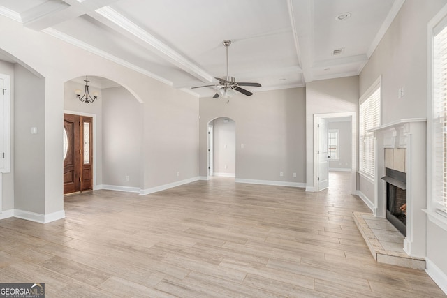 unfurnished living room featuring light wood finished floors, ceiling fan with notable chandelier, beam ceiling, arched walkways, and a warm lit fireplace