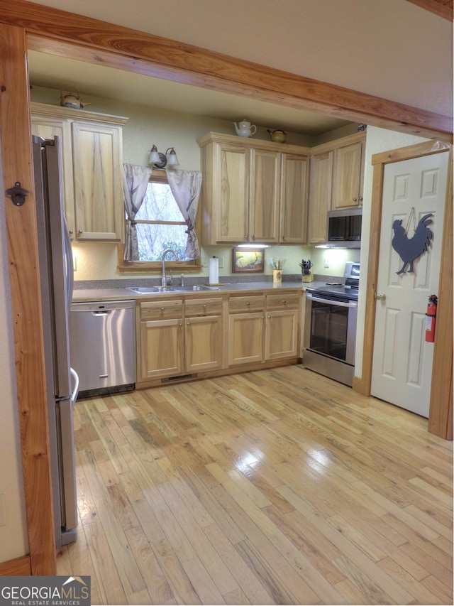 kitchen featuring stainless steel appliances, light wood-style flooring, light brown cabinetry, and a sink