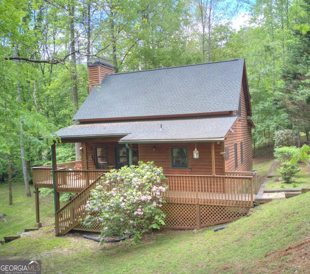 back of property with stairs, a wooden deck, a chimney, a lawn, and a shingled roof