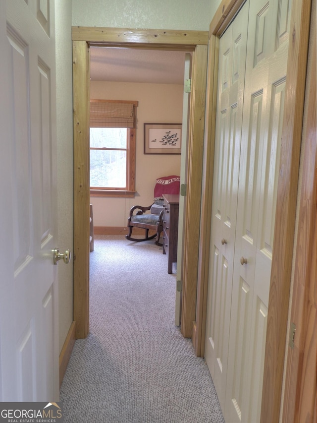 corridor with baseboards and light colored carpet