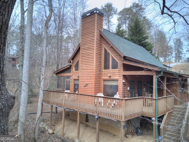 rear view of property with roof with shingles, a chimney, and a wooden deck