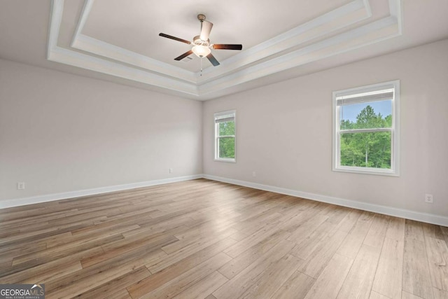 unfurnished room featuring a raised ceiling, baseboards, light wood-style flooring, and a ceiling fan