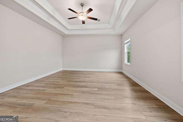 empty room with a tray ceiling, light wood-type flooring, a ceiling fan, and ornamental molding