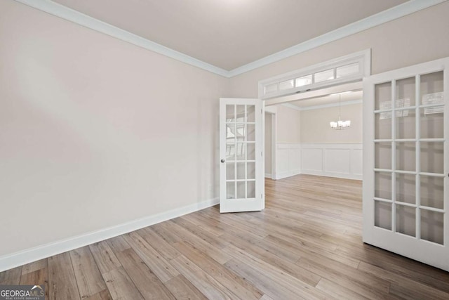 unfurnished room with french doors, wood finished floors, a decorative wall, a chandelier, and ornamental molding