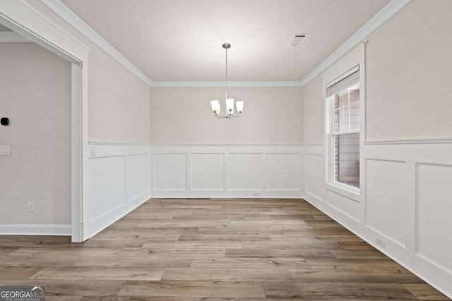 unfurnished dining area with wood finished floors, a notable chandelier, crown molding, a decorative wall, and wainscoting