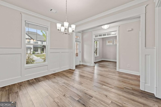 unfurnished dining area with ornamental molding, an inviting chandelier, visible vents, a wainscoted wall, and light wood-style floors
