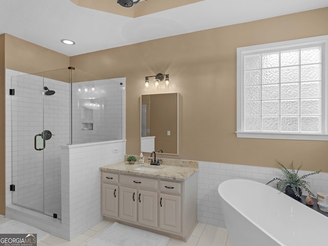 full bathroom featuring tile walls, a wainscoted wall, vanity, a shower stall, and a soaking tub