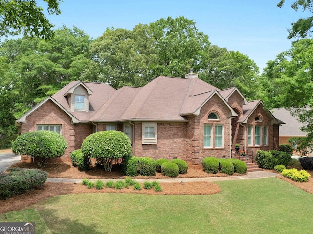 view of front facade featuring a front lawn, brick siding, roof with shingles, and a chimney