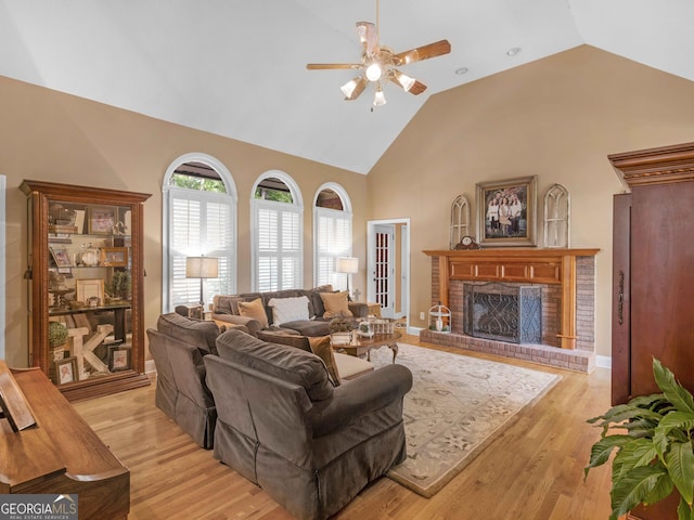 living area featuring light wood finished floors, a brick fireplace, ceiling fan, and high vaulted ceiling