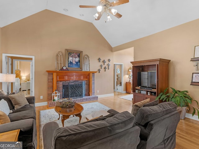 living room featuring baseboards, ceiling fan, a brick fireplace, high vaulted ceiling, and light wood-style floors