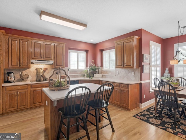 kitchen with brown cabinets, a healthy amount of sunlight, light countertops, and under cabinet range hood