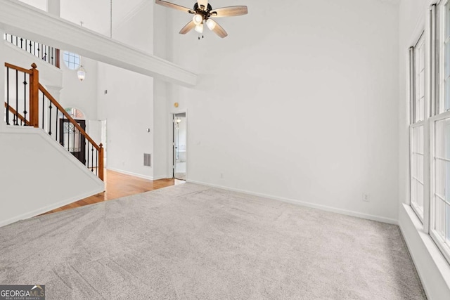 unfurnished living room featuring carpet, stairway, ceiling fan, a high ceiling, and baseboards