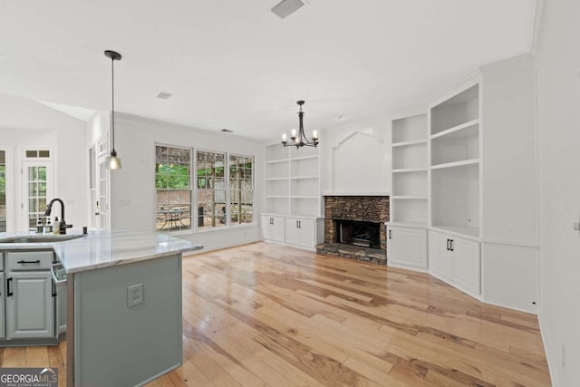 kitchen with an inviting chandelier, light wood-style flooring, a sink, gray cabinetry, and built in shelves