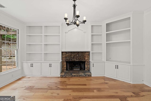 unfurnished living room with an inviting chandelier, light wood-type flooring, built in shelves, and baseboards