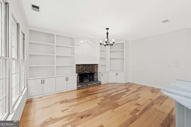 unfurnished living room featuring ornamental molding, light wood finished floors, an inviting chandelier, visible vents, and built in features
