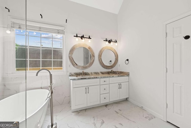 full bathroom with double vanity, marble finish floor, a freestanding tub, and a sink