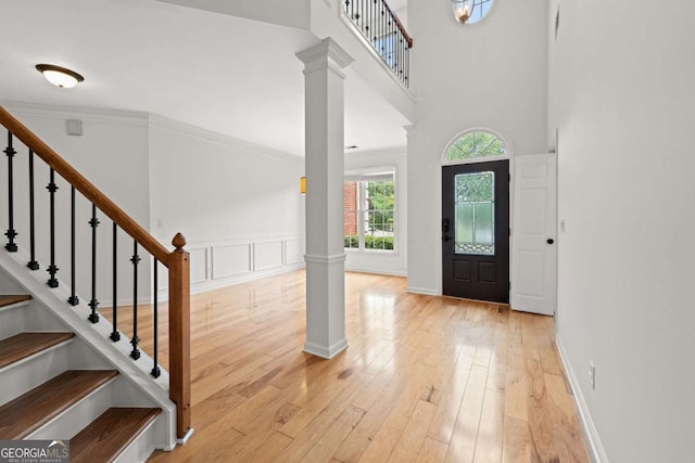 entryway with a towering ceiling, light wood-style flooring, decorative columns, and stairs