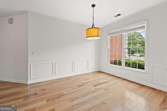 unfurnished dining area with ornamental molding, light wood-style flooring, visible vents, and a wainscoted wall