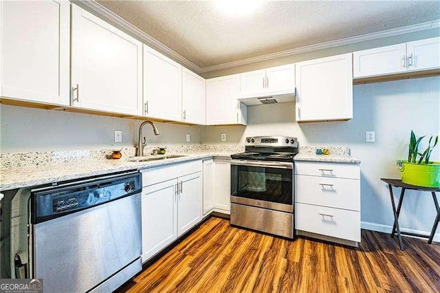 kitchen with under cabinet range hood, ornamental molding, a sink, white cabinets, and appliances with stainless steel finishes