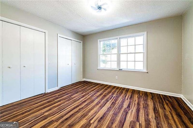 unfurnished bedroom featuring a textured ceiling, dark wood-style flooring, baseboards, and multiple closets