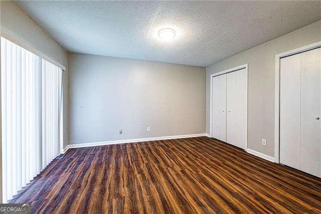 unfurnished bedroom featuring baseboards, dark wood finished floors, two closets, and a textured ceiling