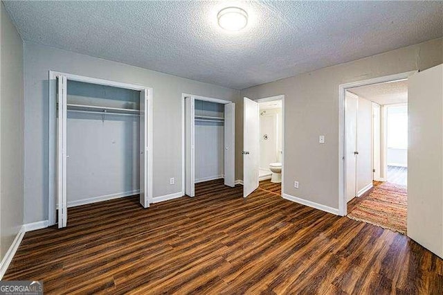 unfurnished bedroom featuring a textured ceiling, two closets, baseboards, and dark wood-style floors