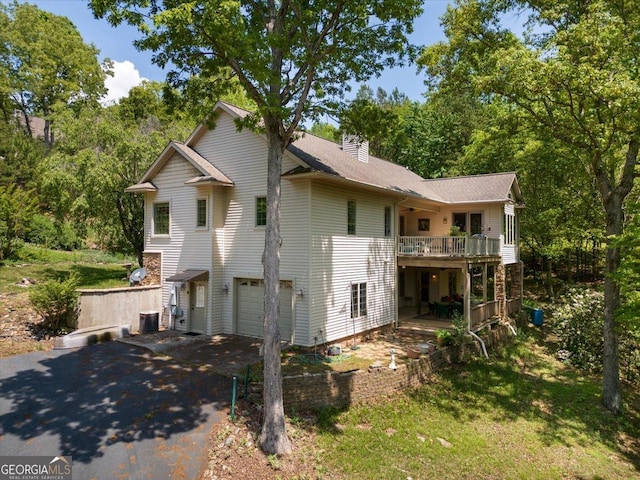 exterior space featuring a deck, an attached garage, driveway, a chimney, and central AC unit