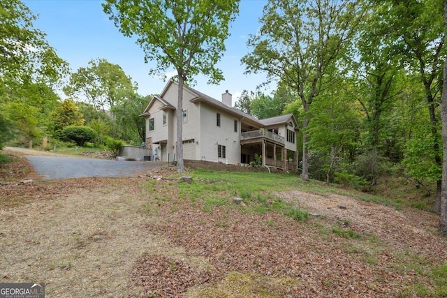 back of property featuring a chimney, driveway, a wooden deck, and a garage