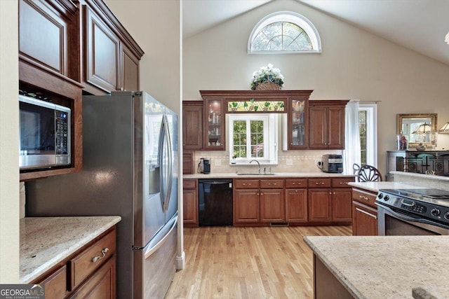 kitchen with high vaulted ceiling, a sink, appliances with stainless steel finishes, backsplash, and light wood-style floors