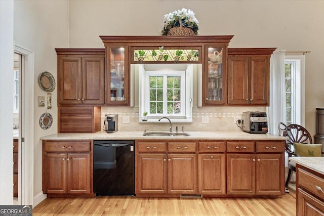 kitchen featuring light wood finished floors, a sink, brown cabinetry, backsplash, and dishwasher