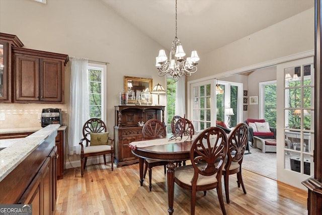 dining space featuring a healthy amount of sunlight, light wood finished floors, a chandelier, and high vaulted ceiling