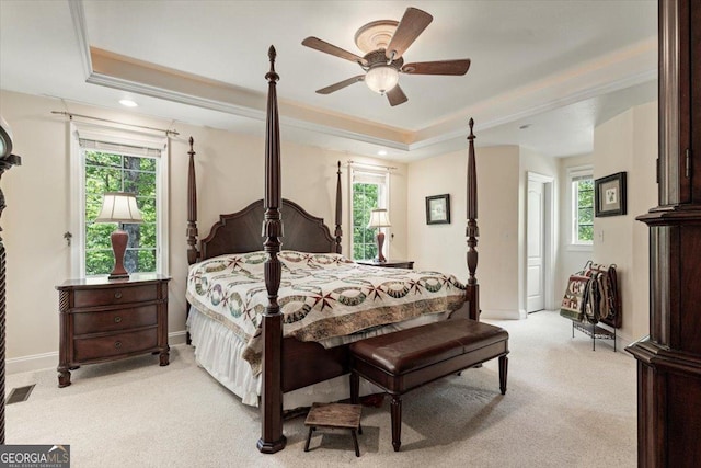 bedroom with a tray ceiling, crown molding, light carpet, and multiple windows