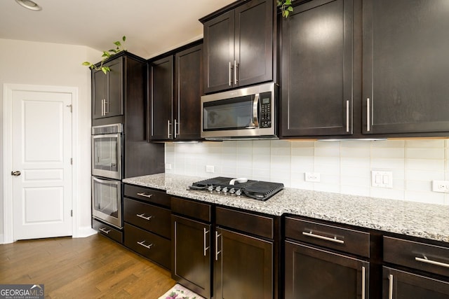 kitchen with appliances with stainless steel finishes, dark wood-style flooring, decorative backsplash, light stone counters, and dark brown cabinetry