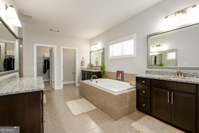 bathroom featuring tile patterned floors, a bath, a spacious closet, two vanities, and baseboards
