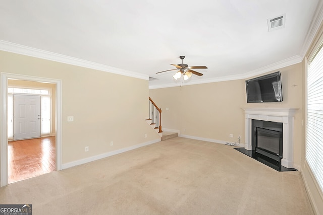 unfurnished living room with ornamental molding, a glass covered fireplace, visible vents, stairway, and light colored carpet