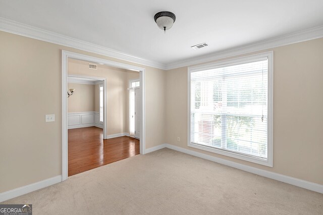 carpeted spare room featuring visible vents, baseboards, and ornamental molding