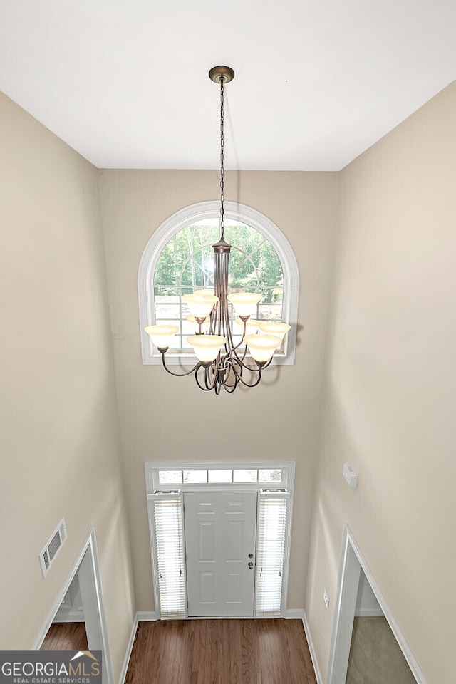 entryway with wood finished floors, visible vents, a chandelier, a high ceiling, and baseboards