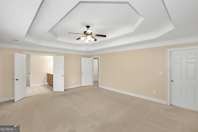 unfurnished bedroom with light carpet, ensuite bath, a tray ceiling, and crown molding