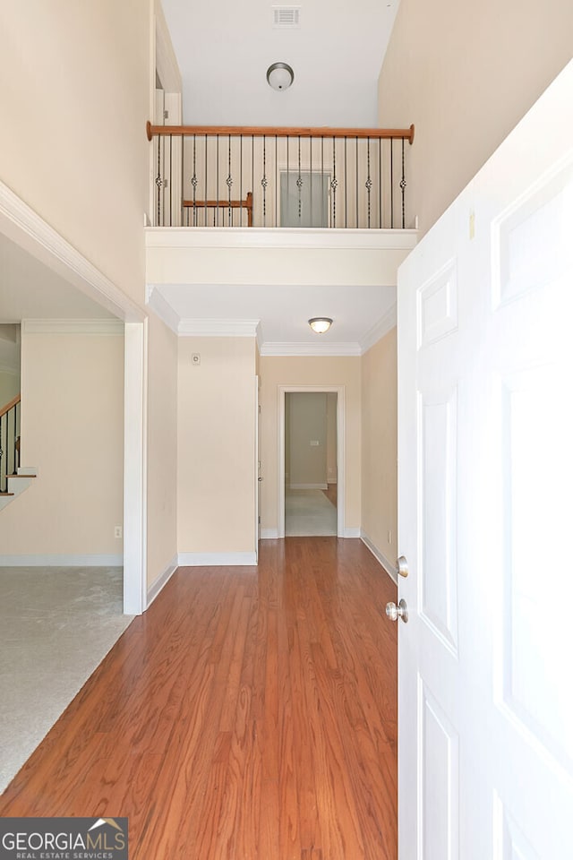 entrance foyer with baseboards, crown molding, a towering ceiling, wood finished floors, and stairway