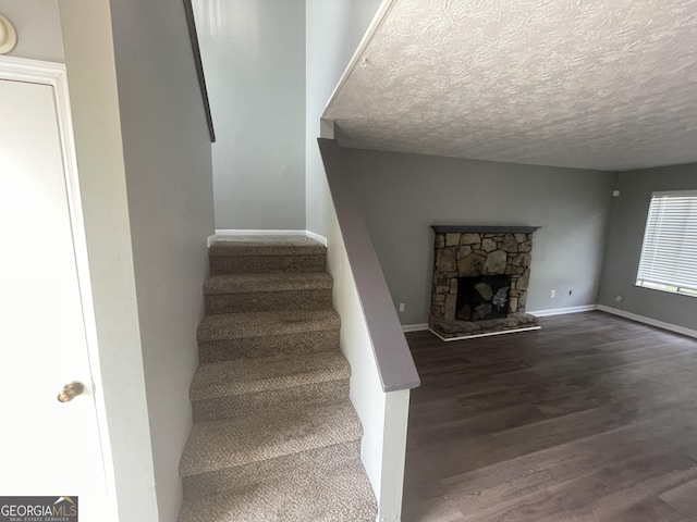 stairs with baseboards, a fireplace, a textured ceiling, and wood finished floors